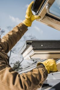 Close up of Caucasian Middle Aged Construction Worker Carefully Checking Fleshly Installed Roof Windows in Newly Built Residential House. Industrial Theme.